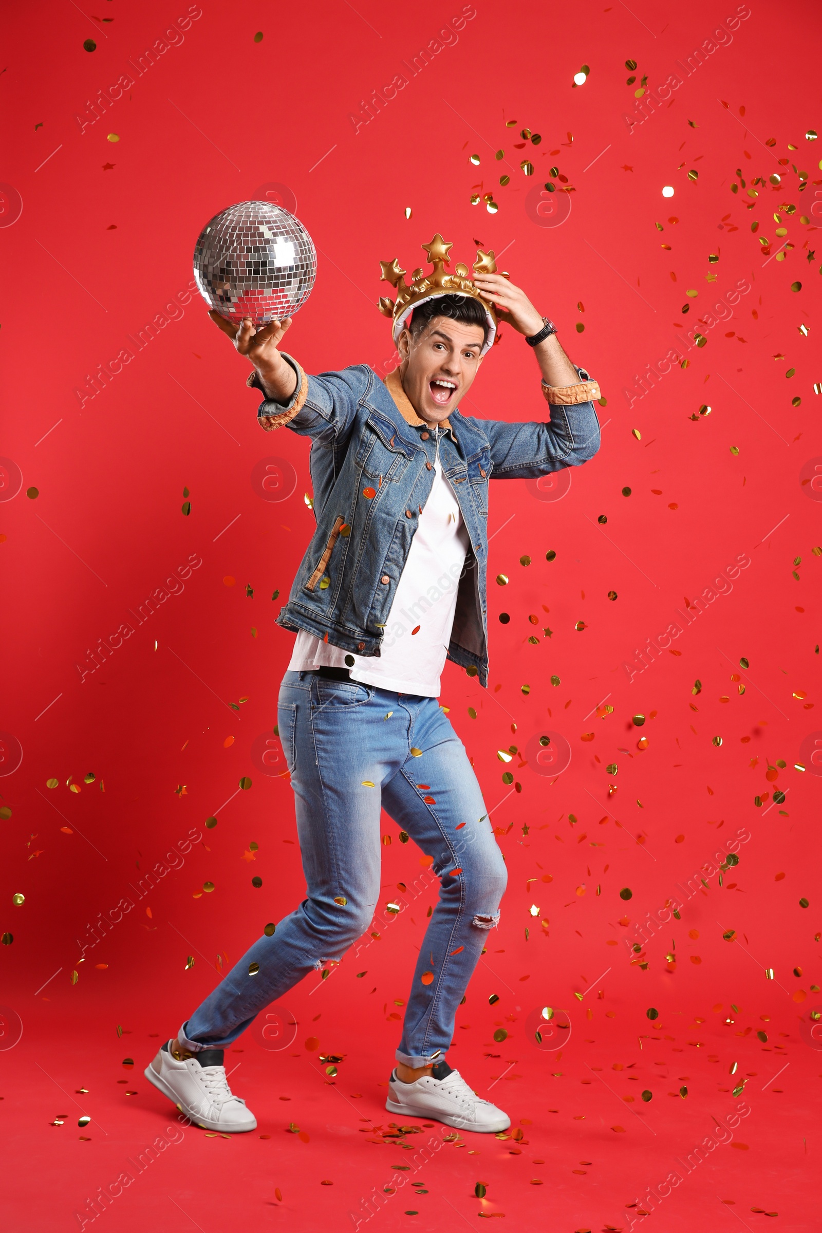 Photo of Happy man in party crown with disco ball and confetti on red background
