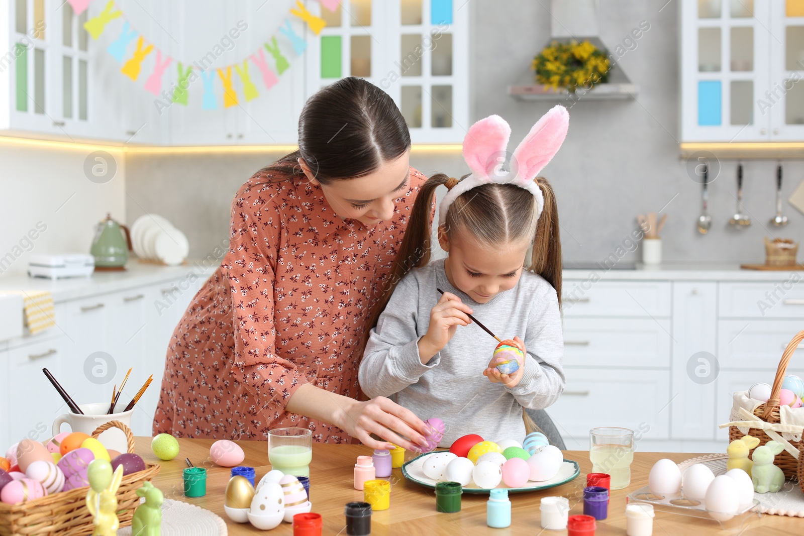 Photo of Mother and her cute daughter painting Easter eggs at table in kitchen