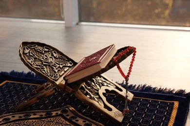 Photo of Rehal with Quran and Muslim prayer beads on rug indoors