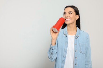 Beautiful happy woman holding red beverage can on light grey background. Space for text