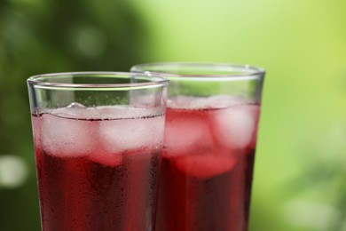 Photo of Refreshing hibiscus tea with ice cubes in glasses on blurred green background, closeup