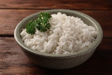 Photo of Delicious rice with parsley in bowl on wooden table, closeup