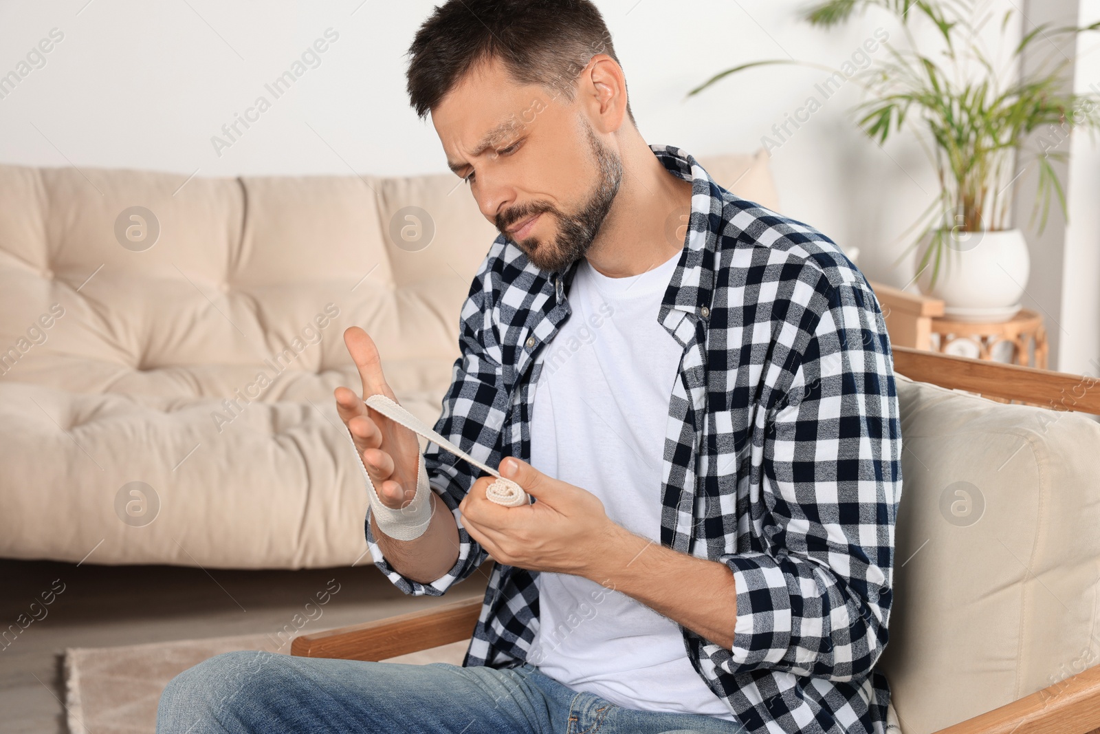 Photo of Man applying medical bandage onto hand at home