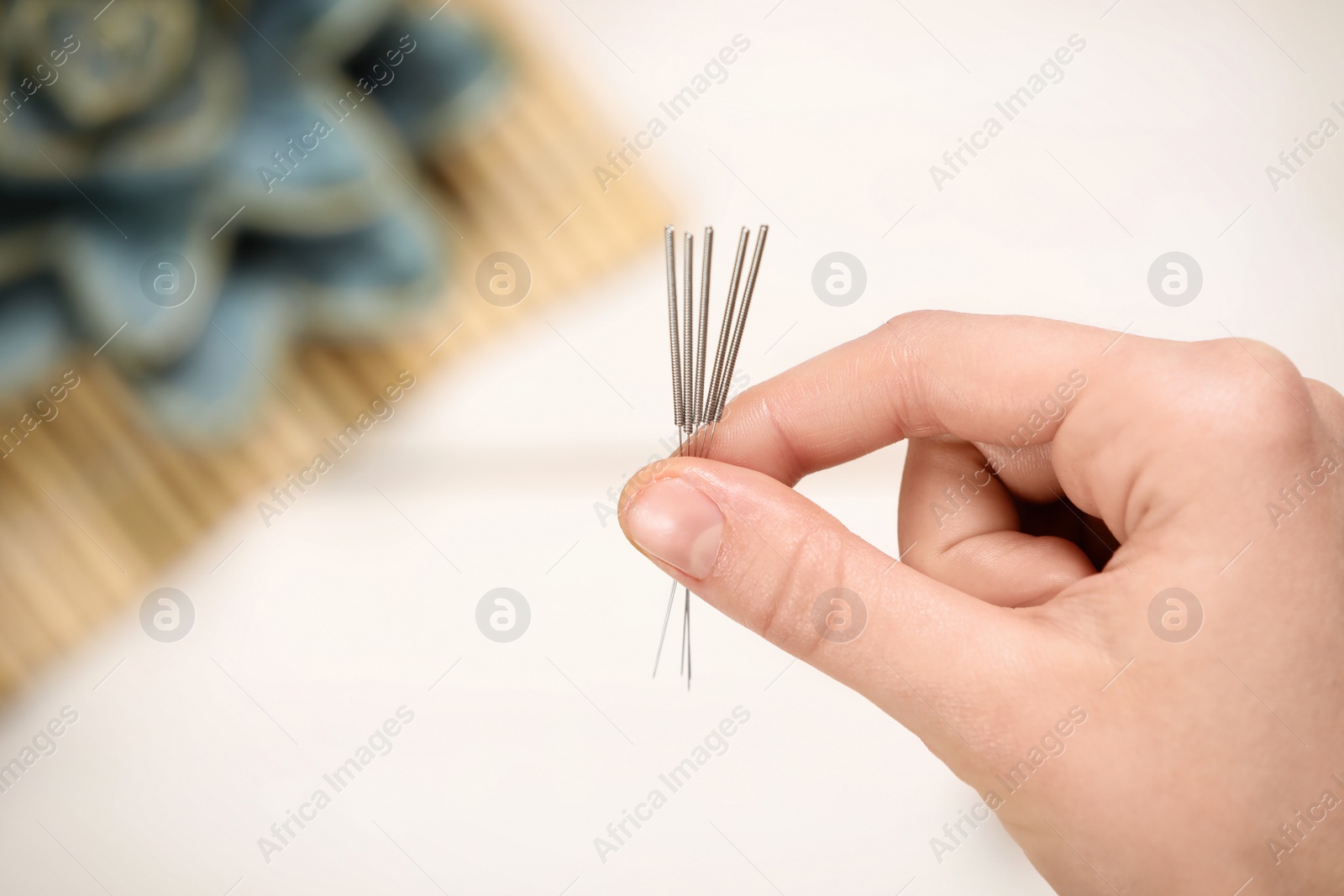 Photo of Woman holding many acupuncture needles over white wooden table, closeup