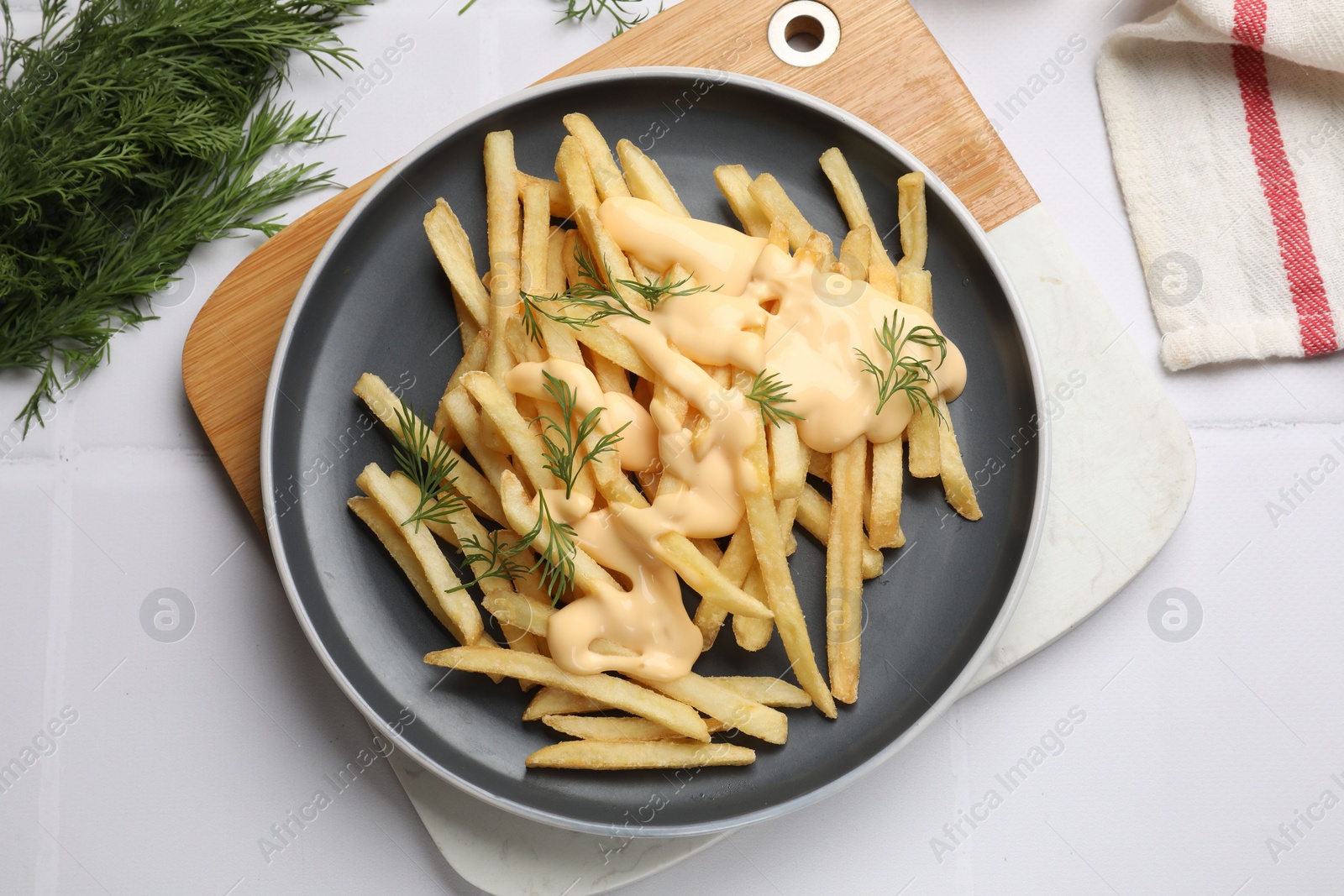 Photo of Delicious french fries with cheese sauce and dill on white tiled table, flat lay