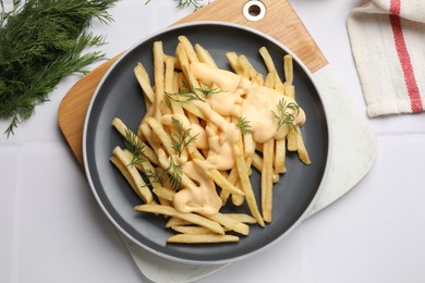 Photo of Delicious french fries with cheese sauce and dill on white tiled table, flat lay