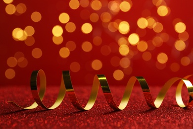 Shiny golden serpentine streamer on red table against blurred lights. Space for text