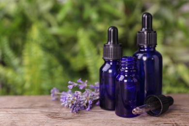 Photo of Bottles with natural lavender essential oil on wooden table against blurred background. Space for text