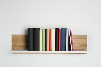 Photo of Different books on wooden shelf near white wall