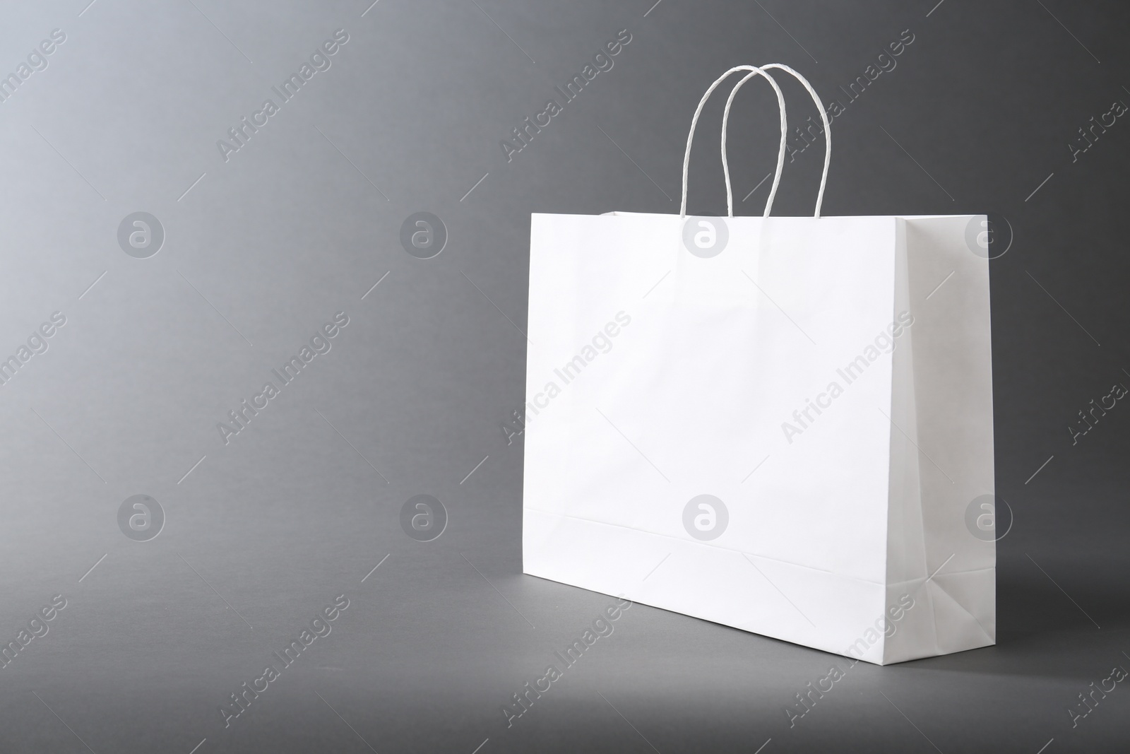 Photo of One white paper bag on grey background, space for text. Mockup for design