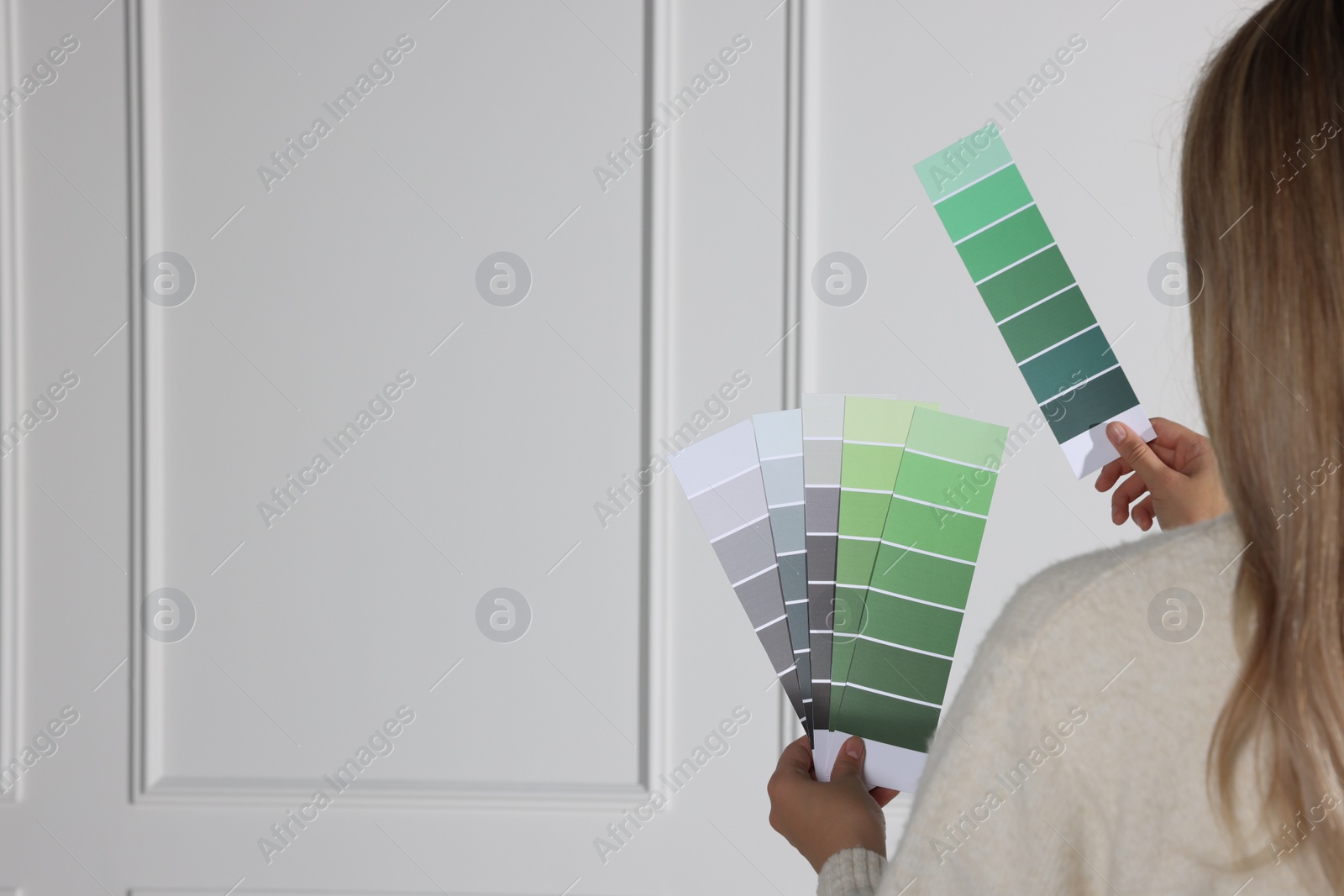 Photo of Woman choosing color for wall indoors, focus on hands with paint chips. Interior design