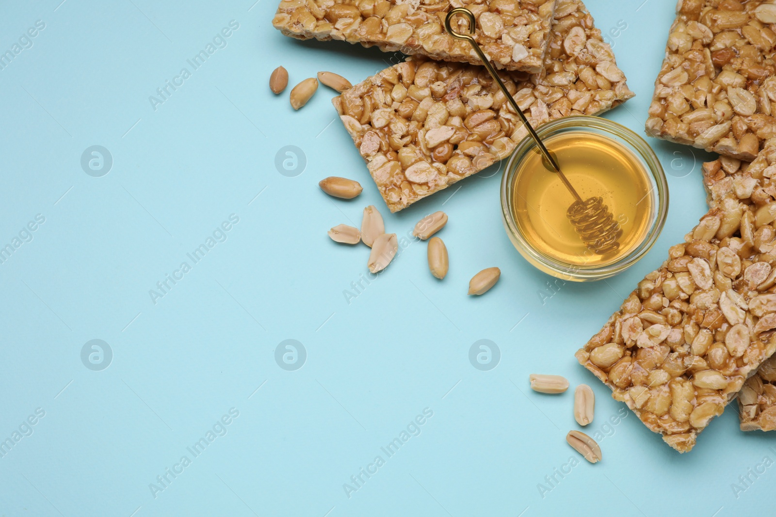 Photo of Tasty kozinaki bars, peanuts and honey on light blue background, flat lay. Space for text