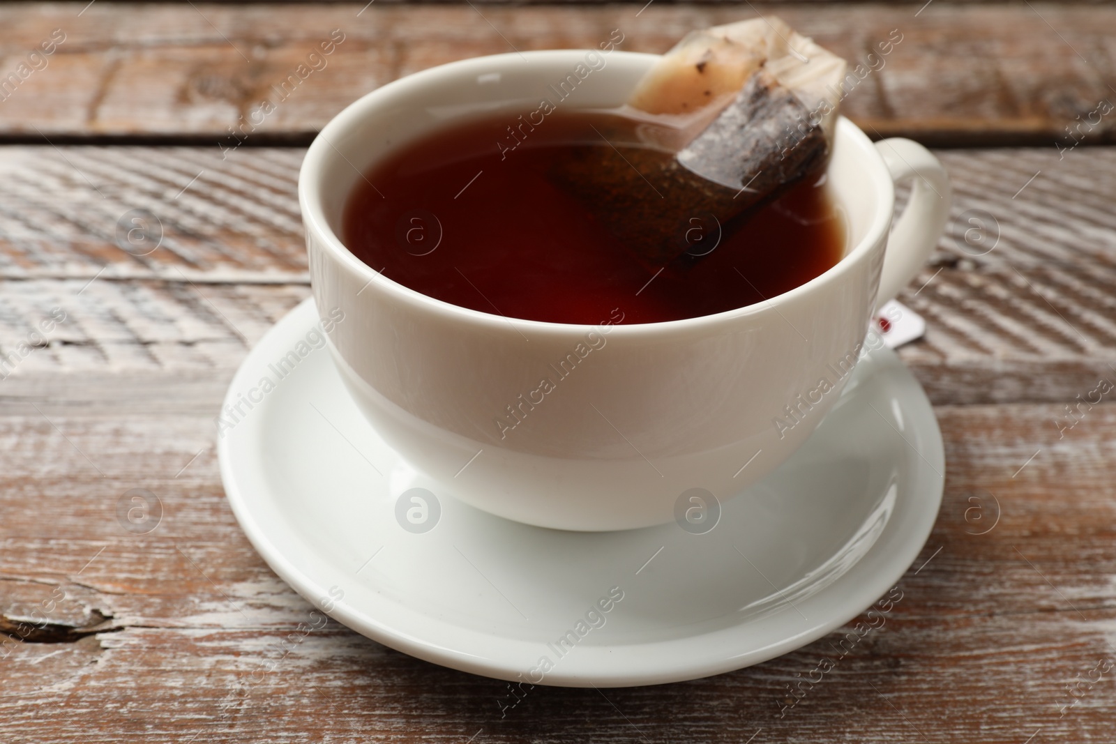 Photo of Tea bag in cup with hot drink on wooden rustic table, closeup