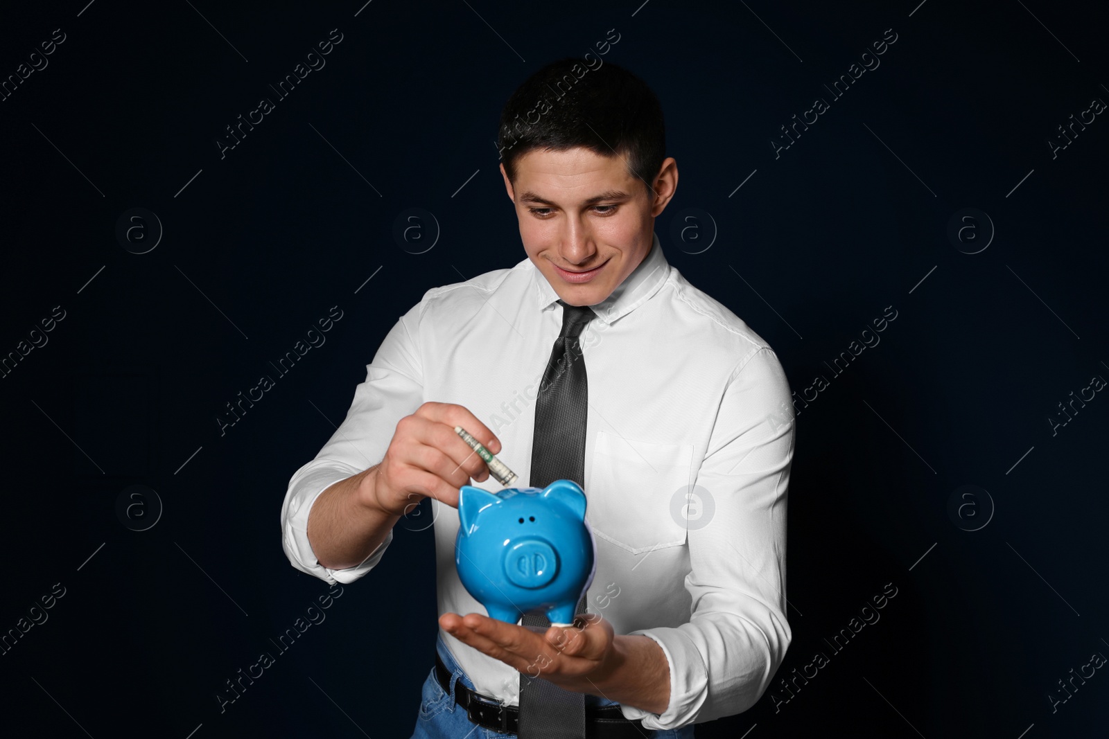 Photo of Businessman putting money into piggy bank on dark background