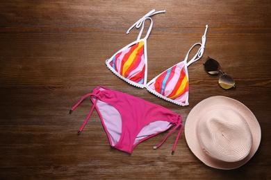 Photo of Beautiful bikini, hat and sunglasses on wooden background, top view