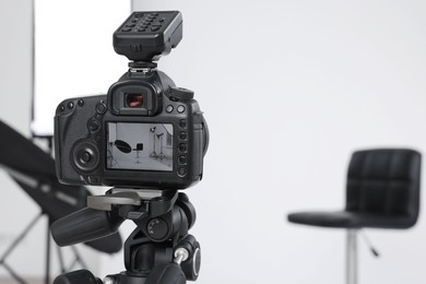 Photo of Tripod with camera, bar stool and professional lighting equipment in modern photo studio, focus on screen. Space for text