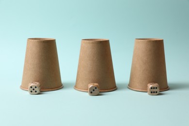 Photo of Three paper cups and dices on light blue background. Thimblerig game