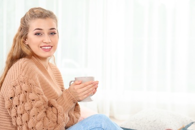 Photo of Attractive young woman in cozy warm sweater with cup of hot drink at home. Space for text
