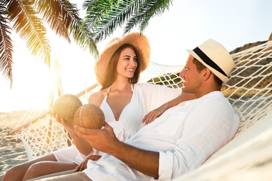 Image of Couple with exotic cocktails relaxing in hammock under green palm leaves on beach