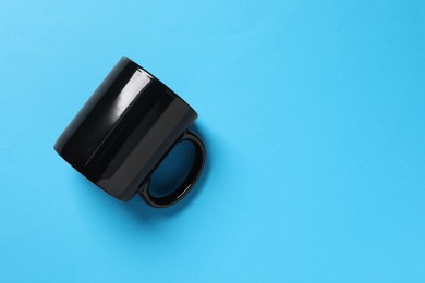 Photo of One black ceramic mug on light blue background, top view. Space for text
