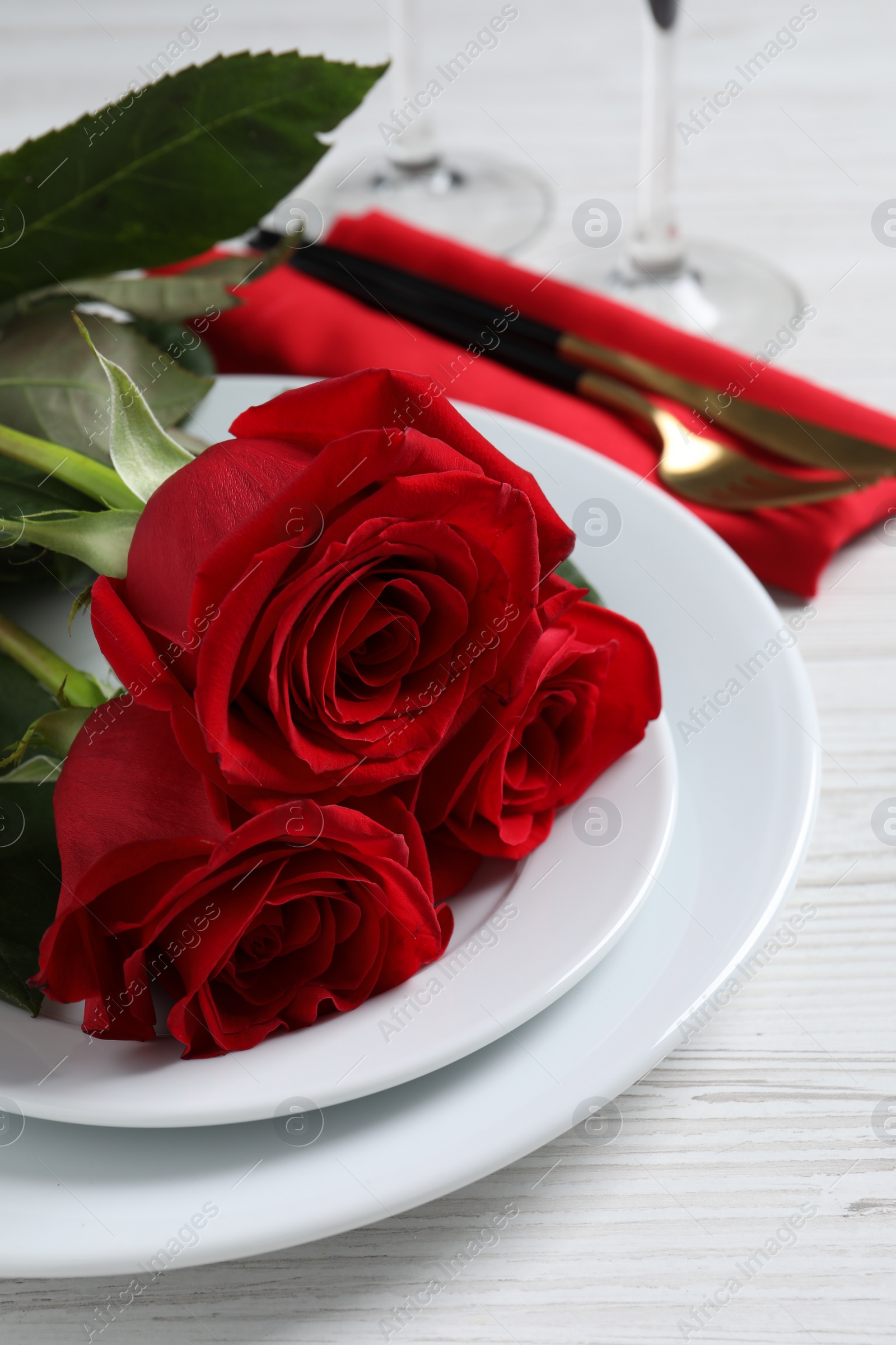 Photo of Beautiful place setting with dishware and roses for romantic dinner on white wooden table, closeup