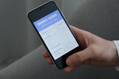 Man holding smartphone with driver's license application form at home, closeup