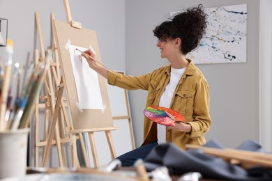 Photo of Young woman painting on easel with paper in studio