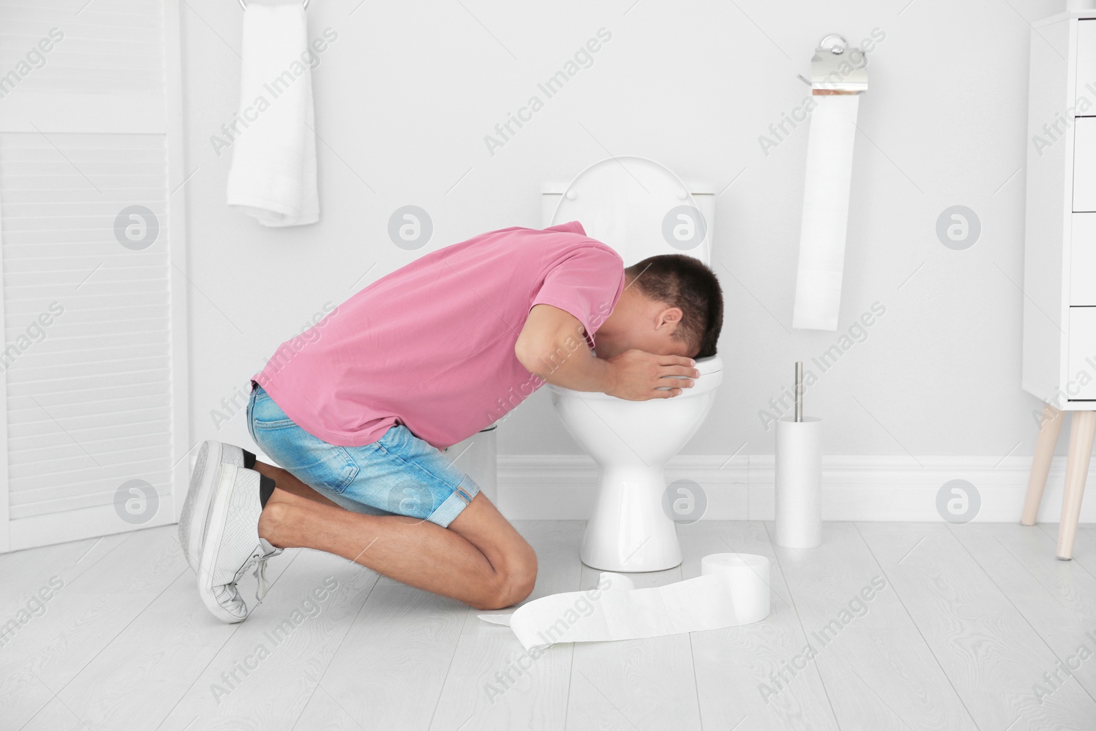 Photo of Young man vomiting in toilet bowl at home