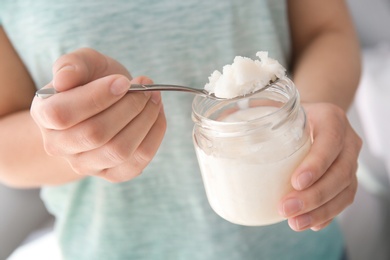 Photo of Woman holding jar and spoon with coconut oil, closeup. Healthy cooking