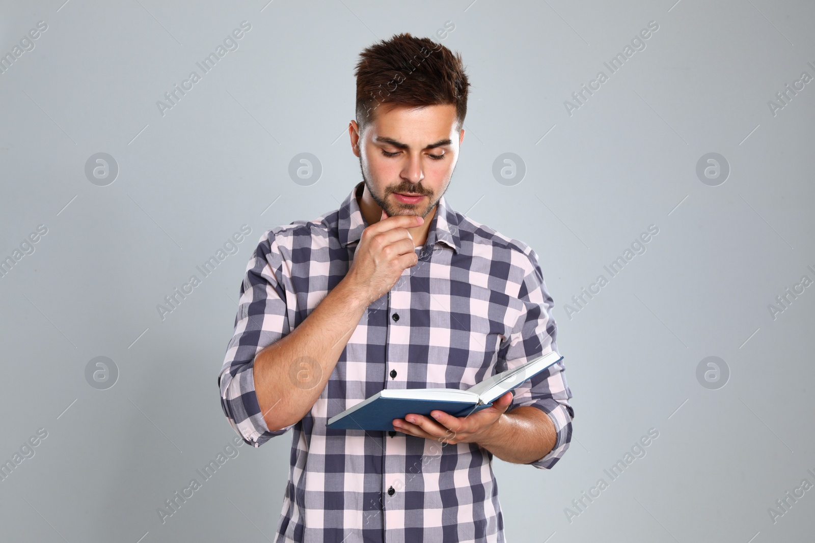 Photo of Handsome young man reading book on light background