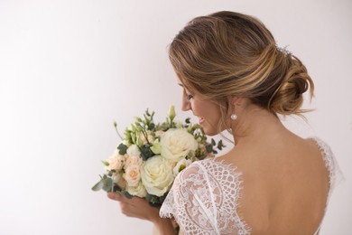 Photo of Young bride with elegant hairstyle holding wedding bouquet on white background