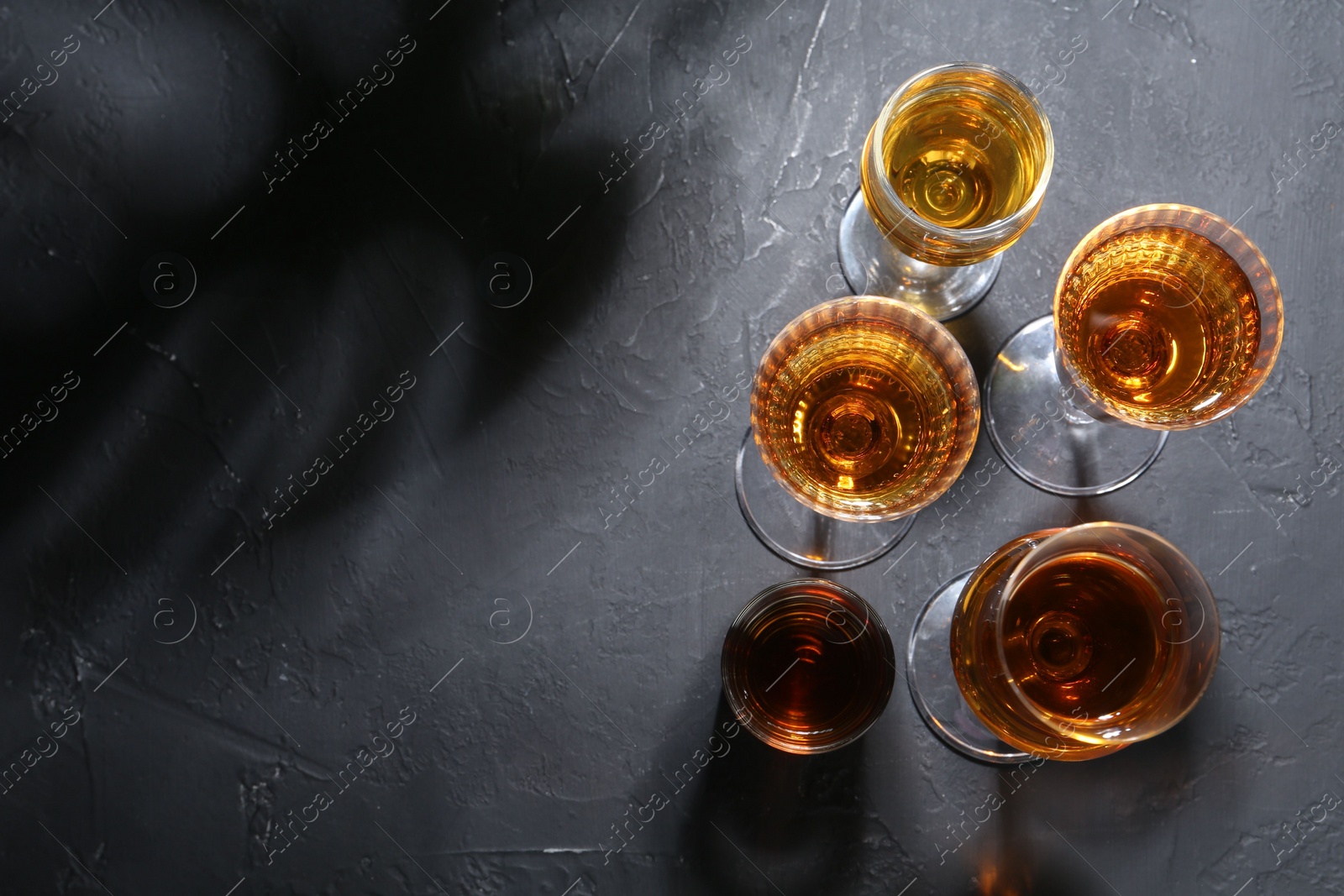 Photo of Many different liqueurs in glasses on dark textured table, flat lay. Space for text