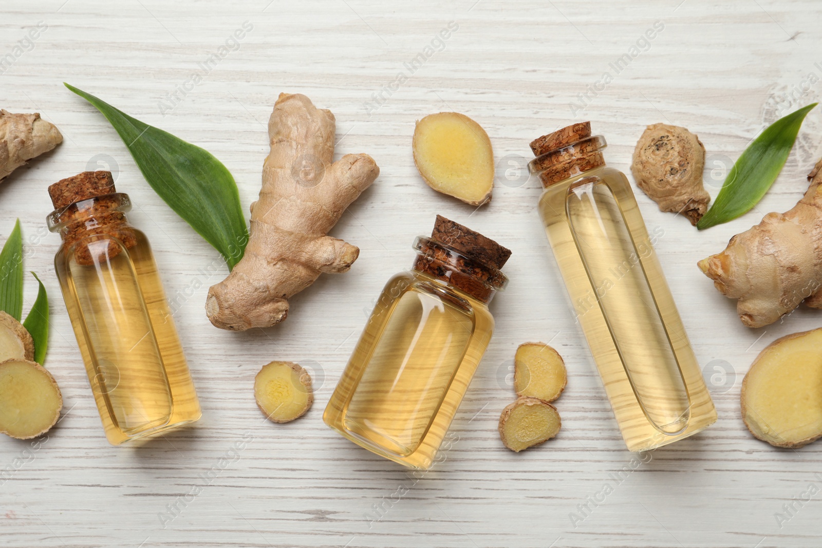 Photo of Glass bottles of essential oil and ginger root on white wooden table, flat lay