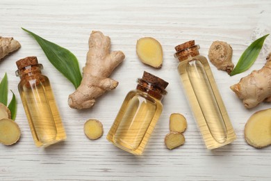 Glass bottles of essential oil and ginger root on white wooden table, flat lay