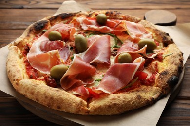 Photo of Tasty pizza with cured ham, olives and sun-dried tomato on wooden table