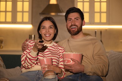 Happy couple watching TV with popcorn on sofa at home