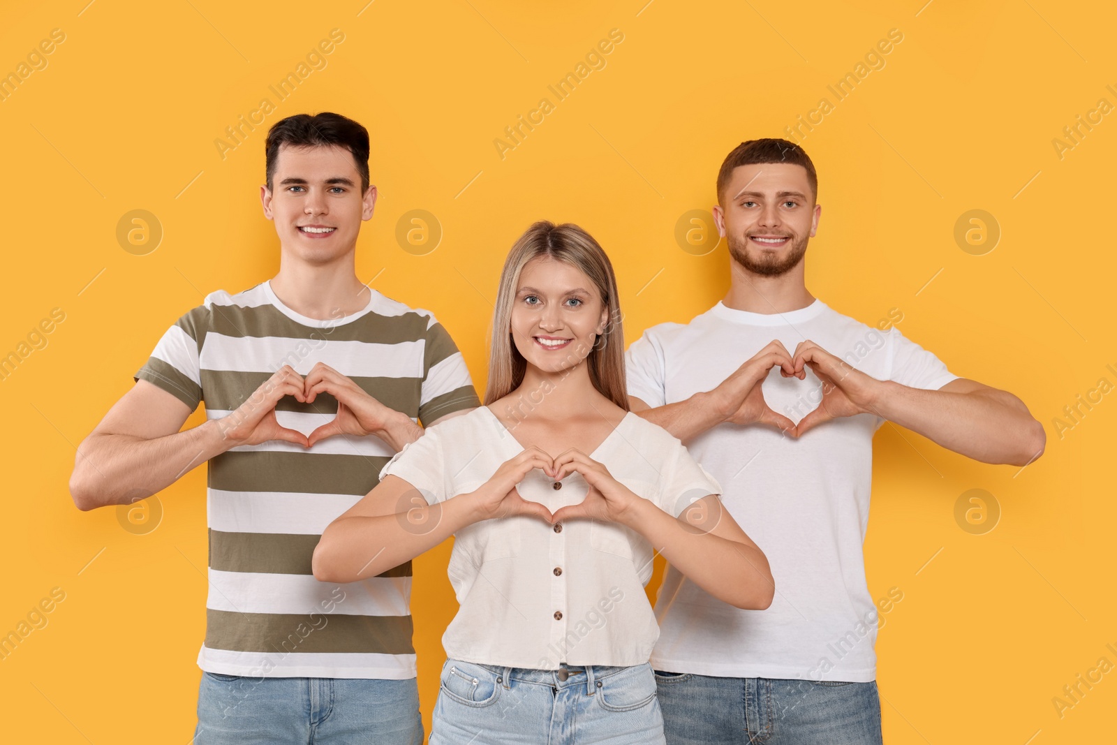 Photo of Happy volunteers making hearts with their hands on orange background