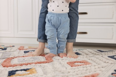 Mother supporting her baby son while he learning to walk on carpet at home, closeup