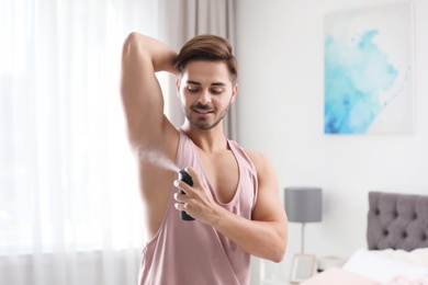 Photo of Handsome young man applying deodorant in bedroom