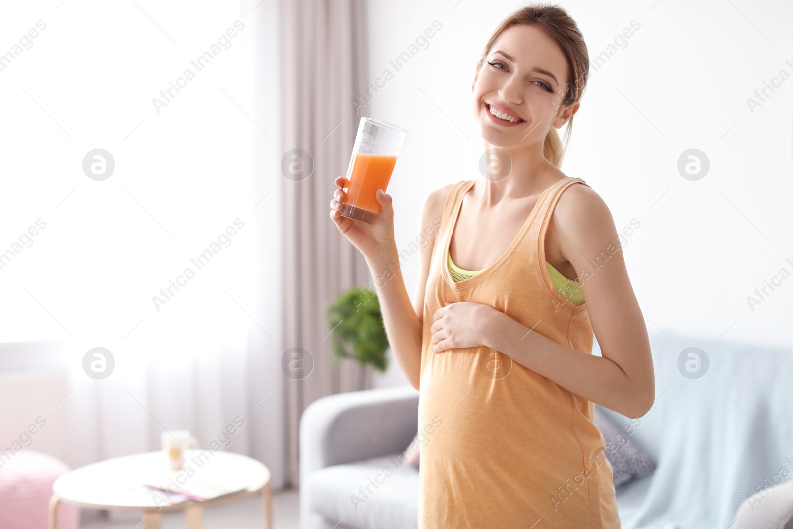 Photo of Young pregnant woman holding glass with juice at home