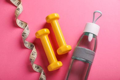 Photo of Measuring tape, bottle of water and dumbbells on pink background, flat lay. Weight control concept