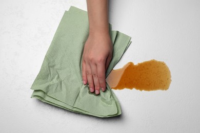 Photo of Woman wiping spilled coffee with paper towel on light table, top view