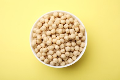 Photo of Tasty cereal balls in bowl on yellow table, top view