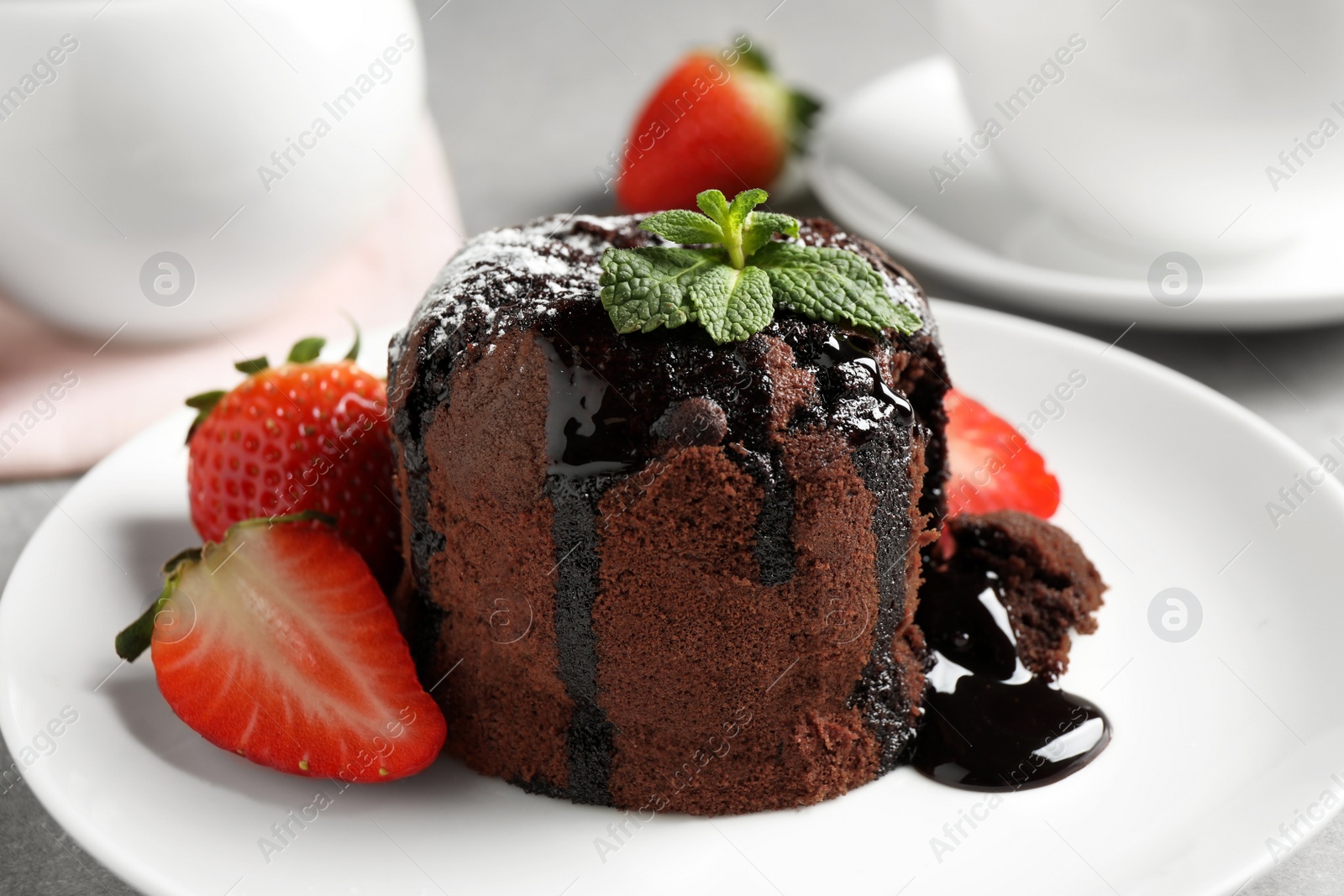 Photo of Delicious warm chocolate lava cake with mint and strawberries on plate, closeup