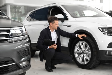 Salesman with clipboard near new car in salon