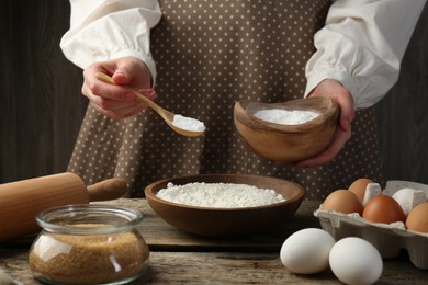 Making dough. Woman adding baking powder to flour at wooden table, closeup