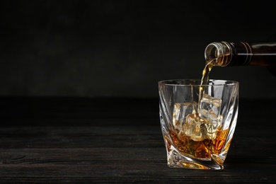 Photo of Pouring whiskey from bottle into glass with ice cubes on table. Space for text