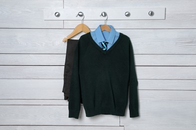 Photo of Shirt, jumper and pants hanging on white wooden wall. School uniform