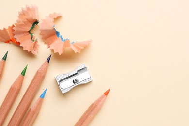 Photo of Colorful pencils, sharpener and shavings on beige background, flat lay. Space for text