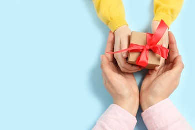 Photo of Mother giving gift box to her child on light blue background, top view. Space for text